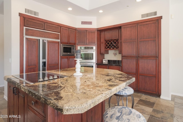 kitchen featuring built in appliances, baseboards, reddish brown cabinets, and visible vents