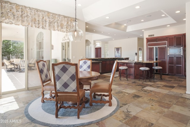 dining space featuring a raised ceiling, arched walkways, recessed lighting, visible vents, and stone tile flooring