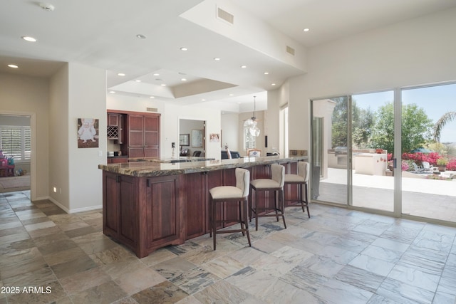 kitchen with a kitchen breakfast bar, visible vents, plenty of natural light, and dark stone countertops