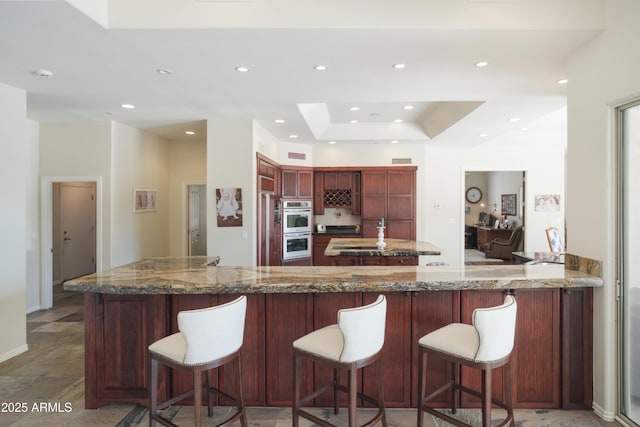 kitchen featuring recessed lighting, a peninsula, stainless steel double oven, and dark brown cabinets
