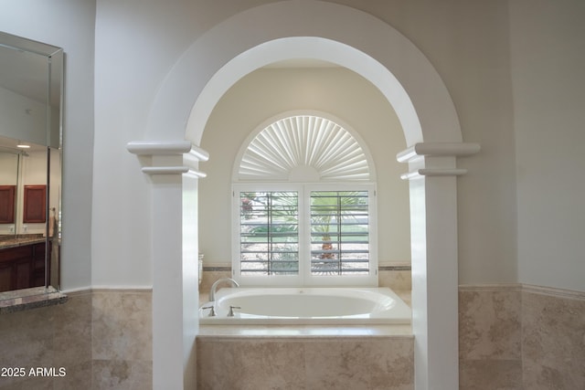 bathroom with tile walls, wainscoting, a garden tub, and vanity