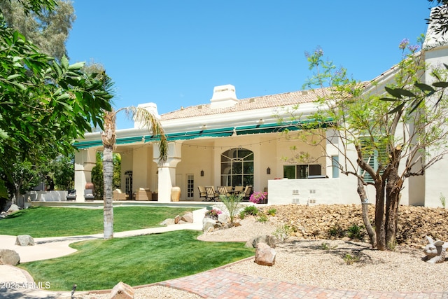rear view of house with a yard, stucco siding, and a chimney