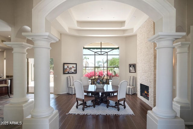 dining room featuring a raised ceiling, a high ceiling, a lit fireplace, and dark wood finished floors