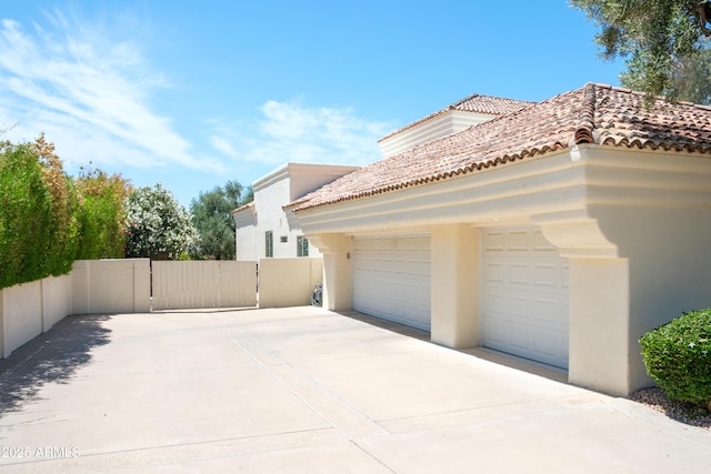 view of side of property featuring an attached garage, stucco siding, a gate, a tiled roof, and driveway