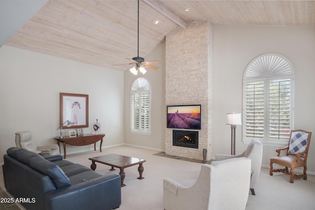 living area featuring beam ceiling, a stone fireplace, baseboards, a ceiling fan, and carpet