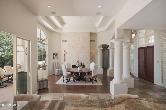dining area featuring a high ceiling, recessed lighting, decorative columns, wood finished floors, and a tray ceiling