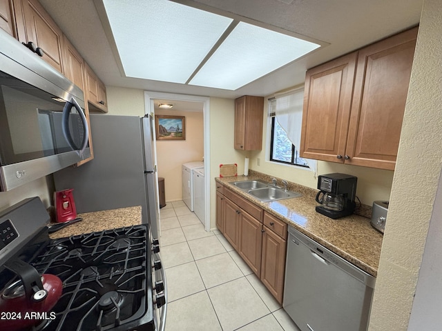 kitchen featuring appliances with stainless steel finishes, washing machine and clothes dryer, light tile patterned flooring, a skylight, and sink