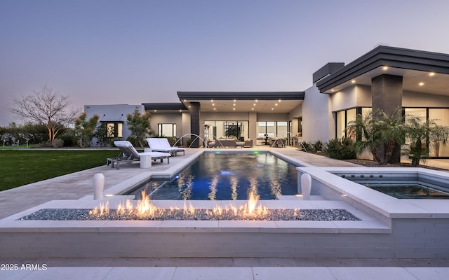 pool at dusk featuring a fire pit, an in ground hot tub, pool water feature, a yard, and a patio area