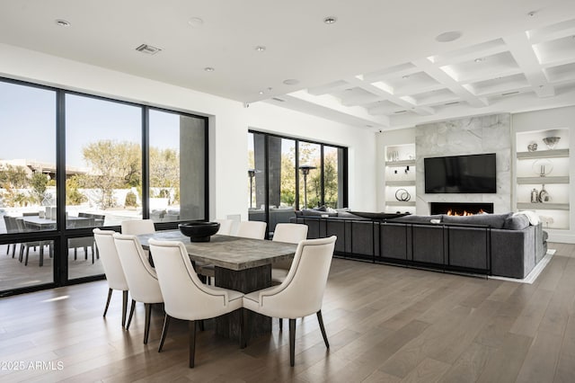 dining area with coffered ceiling, beam ceiling, wood-type flooring, and a premium fireplace