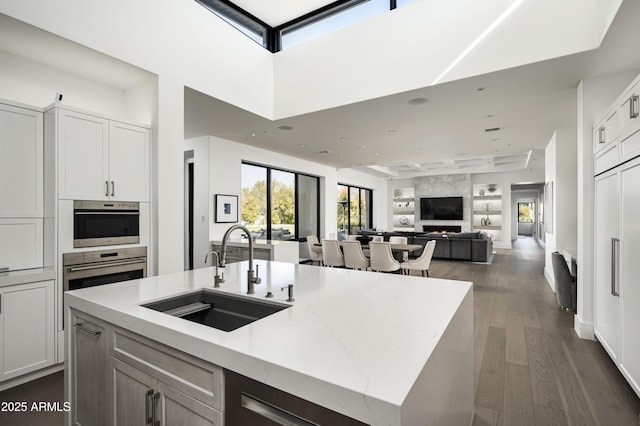 kitchen with dark hardwood / wood-style floors, white cabinetry, an island with sink, sink, and light stone countertops