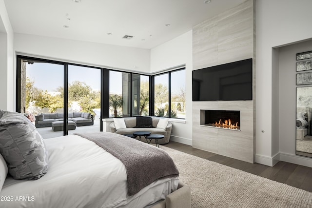 bedroom with a tiled fireplace, dark hardwood / wood-style floors, access to outside, and a towering ceiling