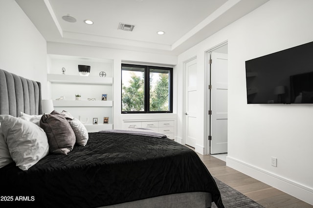 bedroom with a raised ceiling and light wood-type flooring