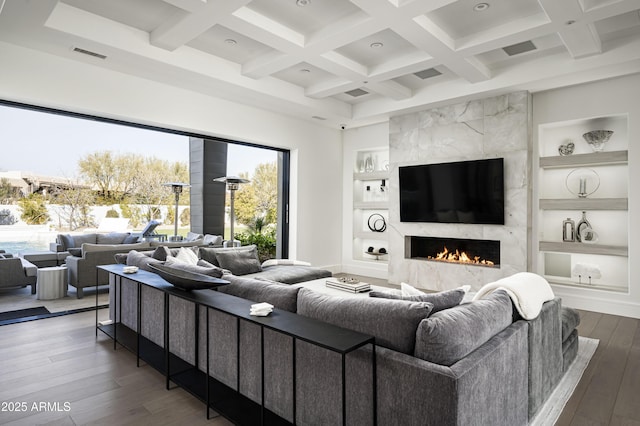 living room featuring coffered ceiling, built in shelves, dark wood-type flooring, and a premium fireplace