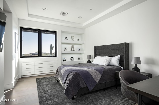 bedroom with a raised ceiling and light wood-type flooring