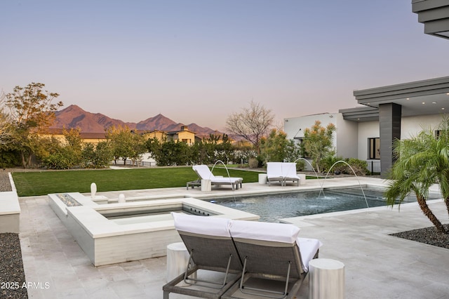 pool at dusk with pool water feature, a patio area, a lawn, an outdoor fire pit, and a mountain view