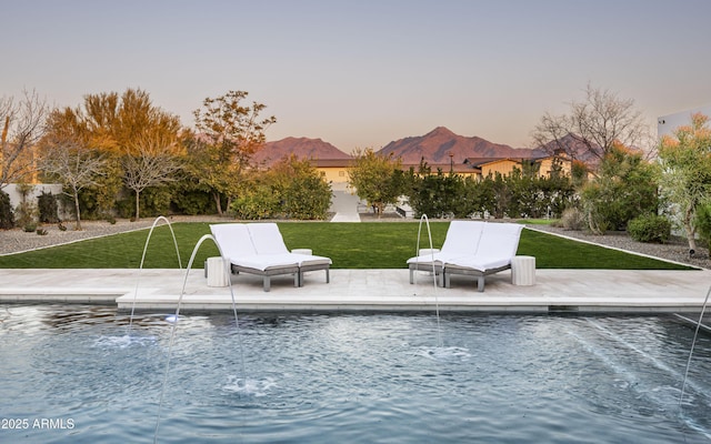 pool at dusk with a yard, a mountain view, and a patio area