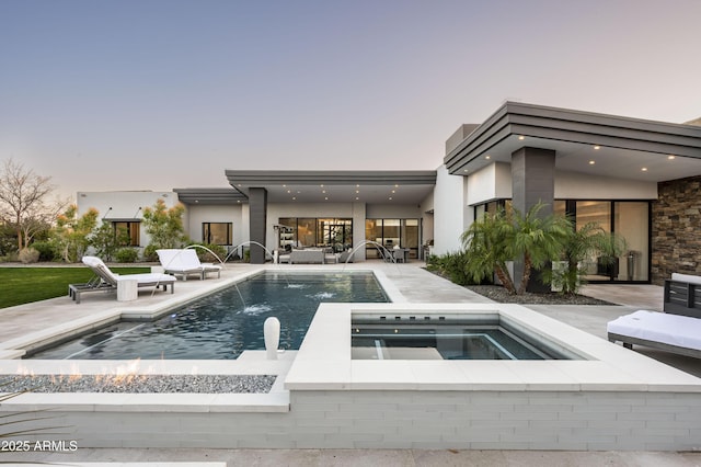 pool at dusk with an in ground hot tub, pool water feature, and a patio