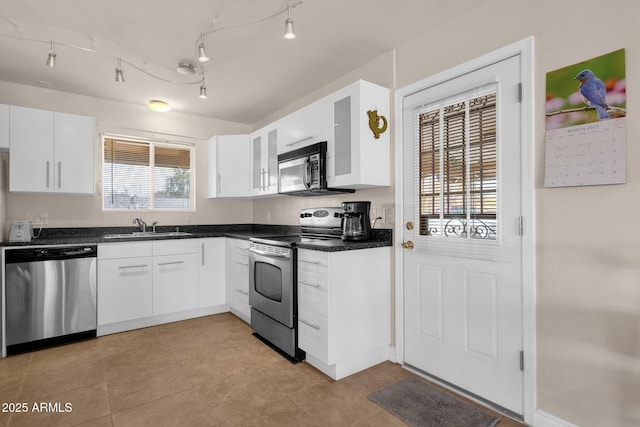 kitchen with white cabinets, dark countertops, glass insert cabinets, appliances with stainless steel finishes, and a sink