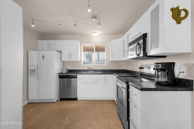 kitchen featuring stainless steel appliances, dark countertops, white cabinets, and a sink