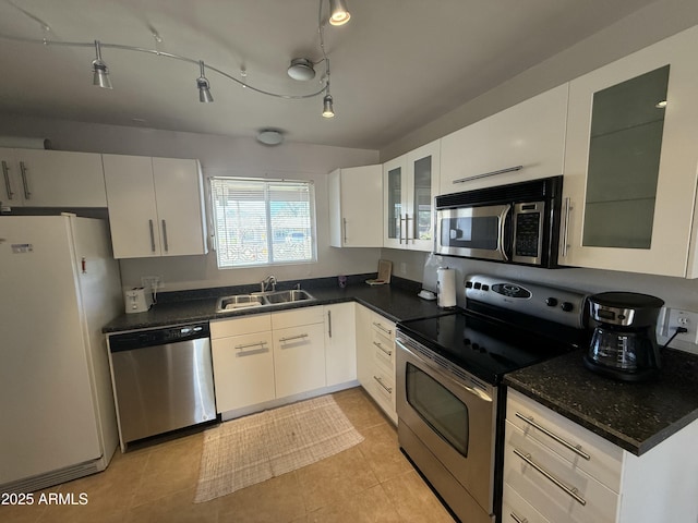 kitchen featuring stainless steel appliances, dark countertops, a sink, and white cabinets