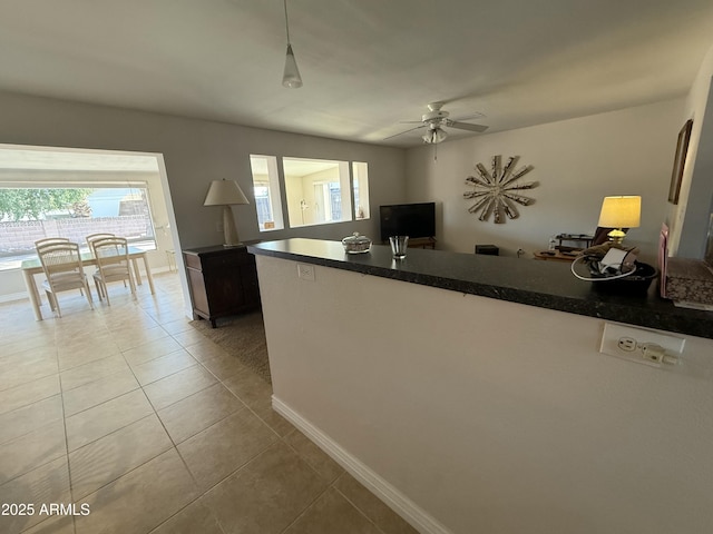 kitchen featuring dark countertops, a ceiling fan, tile patterned flooring, a peninsula, and baseboards