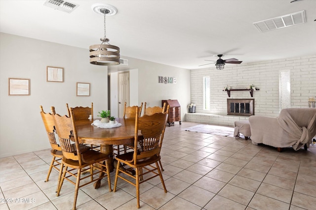 dining space featuring light tile patterned floors, brick wall, a brick fireplace, and ceiling fan