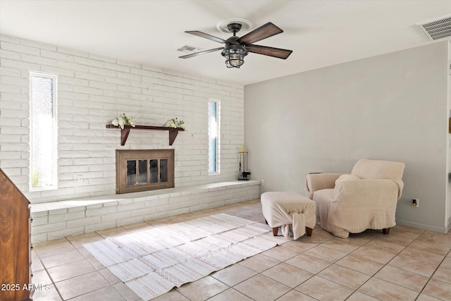 unfurnished room featuring ceiling fan, a wealth of natural light, a brick fireplace, and light tile patterned floors