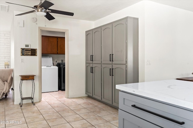 kitchen with light tile patterned floors, gray cabinets, ceiling fan, light stone counters, and separate washer and dryer