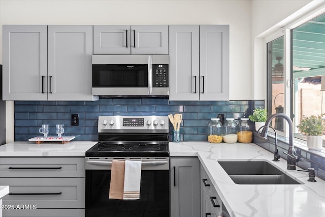 kitchen featuring sink, tasteful backsplash, gray cabinets, stainless steel appliances, and light stone countertops