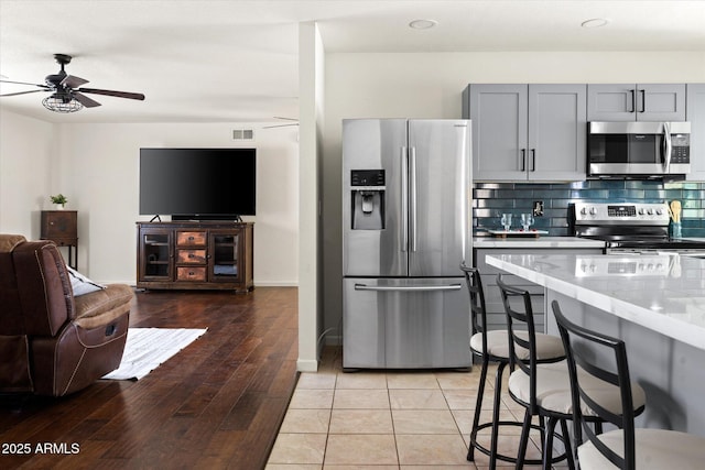 kitchen with stainless steel appliances, light stone countertops, gray cabinets, and backsplash