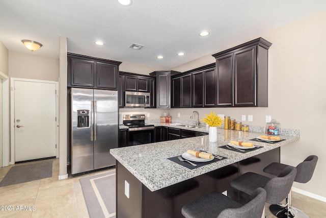 kitchen featuring sink, dark brown cabinets, stainless steel appliances, light stone countertops, and kitchen peninsula