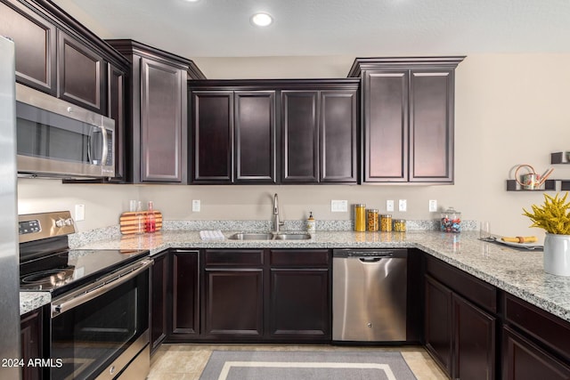 kitchen with dark brown cabinetry, appliances with stainless steel finishes, light stone countertops, and sink