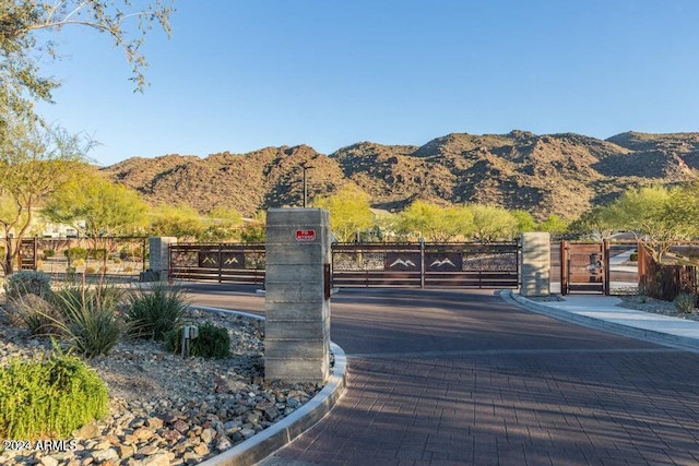 view of road featuring a mountain view, curbs, a gated entry, and a gate