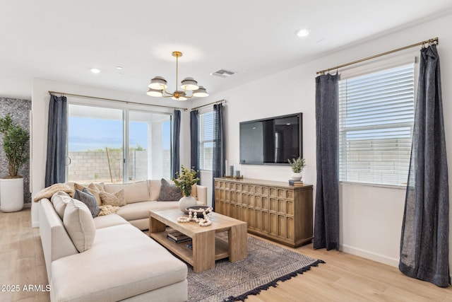 living area with a chandelier, light wood-style flooring, visible vents, and baseboards