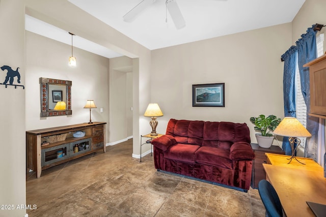 living room featuring ceiling fan, stone finish flooring, and baseboards
