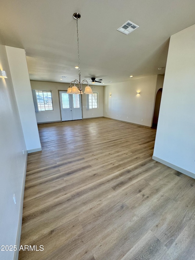 spare room featuring baseboards, visible vents, arched walkways, wood finished floors, and ceiling fan with notable chandelier