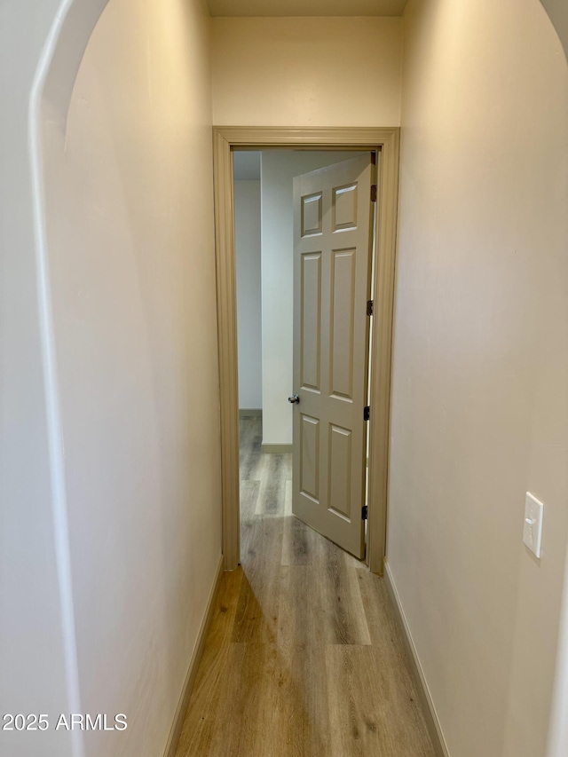 hall featuring baseboards, arched walkways, and wood finished floors