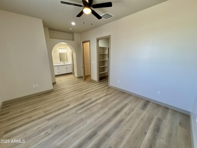 unfurnished bedroom with arched walkways, visible vents, baseboards, a spacious closet, and light wood-type flooring