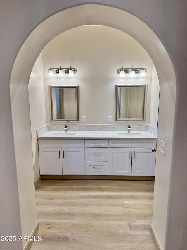 full bath with double vanity, a sink, baseboards, and wood finished floors