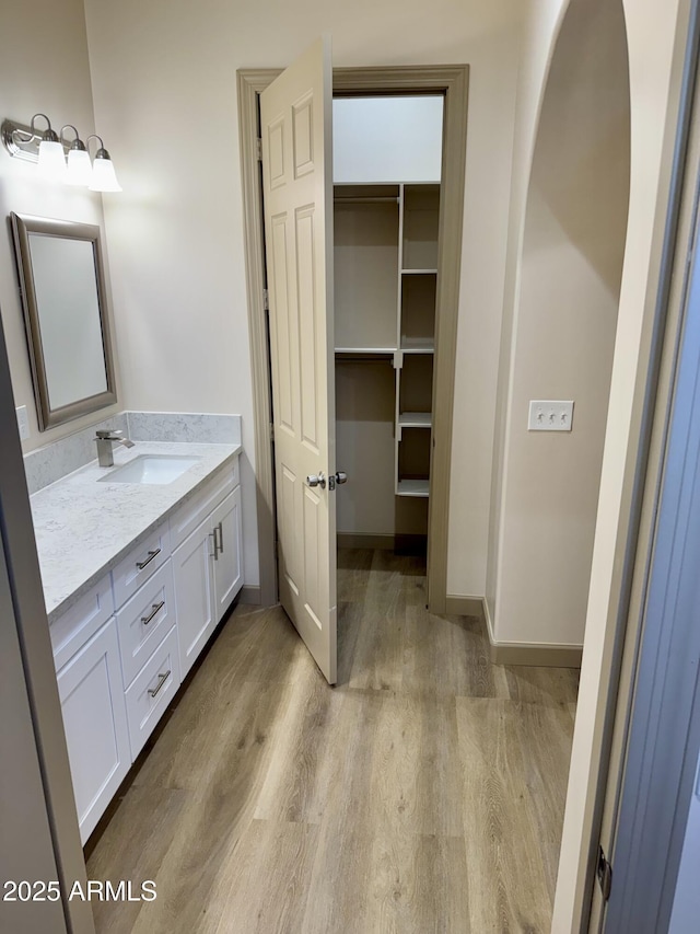 bathroom with baseboards, a walk in closet, wood finished floors, and vanity