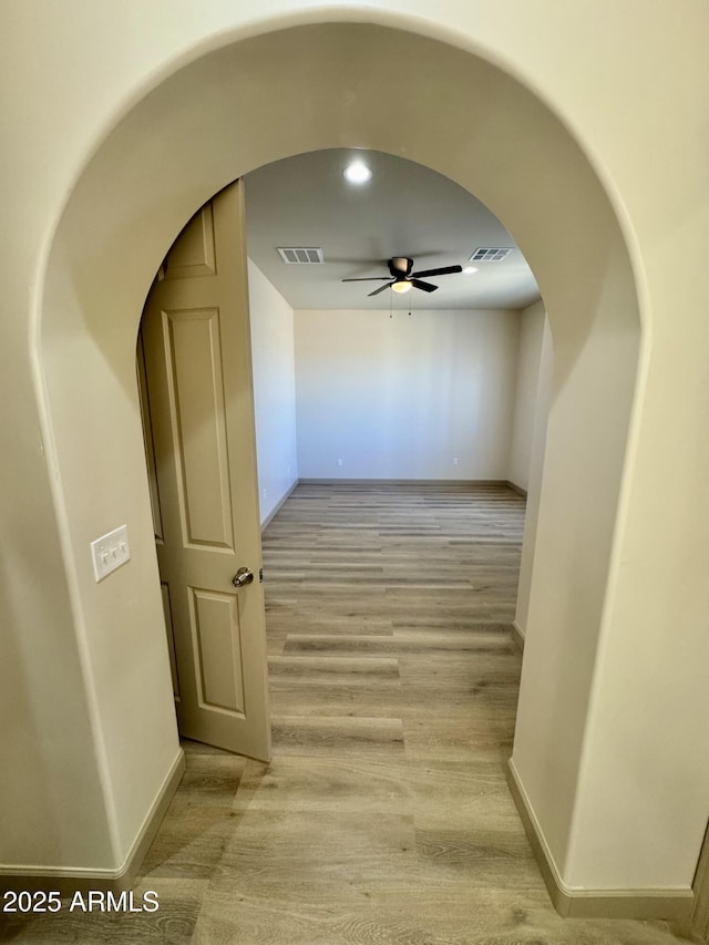 corridor featuring arched walkways, baseboards, visible vents, and light wood finished floors