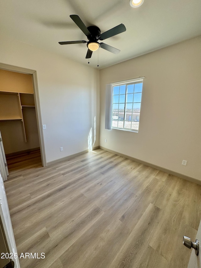 unfurnished bedroom with light wood finished floors, baseboards, a walk in closet, and a ceiling fan