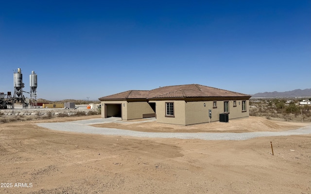 rear view of house with stucco siding, an attached garage, central AC unit, driveway, and a tiled roof