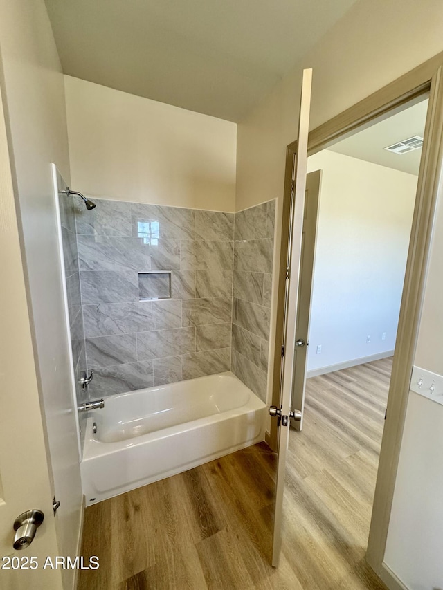 bathroom featuring bathing tub / shower combination, wood finished floors, visible vents, and baseboards