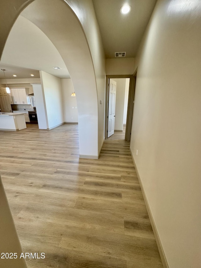 corridor featuring arched walkways, light wood-style flooring, and visible vents