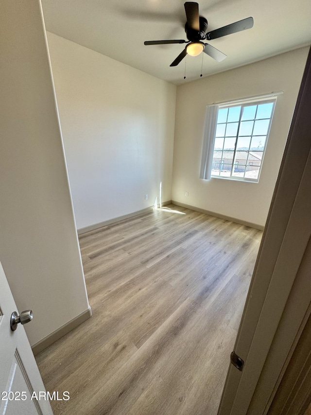 empty room with ceiling fan, light wood-style flooring, and baseboards