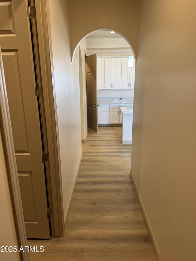 hallway with arched walkways, light wood-style flooring, and baseboards