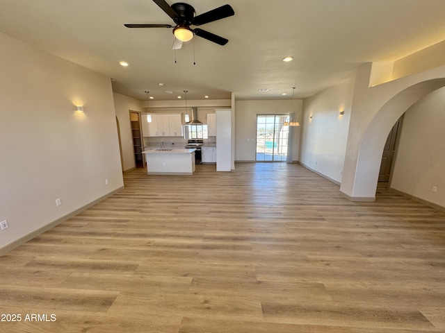 unfurnished living room with light wood-style floors, arched walkways, recessed lighting, and ceiling fan with notable chandelier