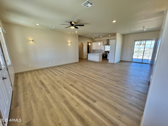 unfurnished living room with arched walkways, recessed lighting, ceiling fan with notable chandelier, visible vents, and light wood finished floors