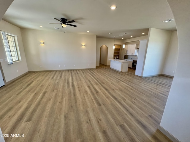 unfurnished living room with visible vents, arched walkways, light wood-style flooring, a sink, and recessed lighting